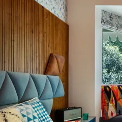 The kids' bedroom at Valley of Dreams is a vibrant ode to playful comfort. The geometric upholstered headboard and fluted wooden panel are paired with a bespoke bay window nook that doubles as storage, sparking joy while grounding the senses in nature.