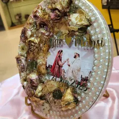 This oval resin frame is a beautiful example of how I can preserve your wedding varmala. I arranged the dried roses and other flowers around the couple's photo and added a border of pearls to create a classic, elegant look. It’s a wonderful centerpiece for a side table.