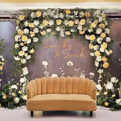 A dreamy engagement stage for Sanika and Sneh, featuring a beautiful arch of white and yellow roses against a soft grey backdrop. The personalized names and delicate floral details create a romantic and welcoming atmosphere.