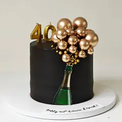 A chic and modern 40th birthday cake with a champagne bottle theme. The design features a cascade of golden chocolate spheres bubbling out of an edible bottle image on a sleek black cake.
