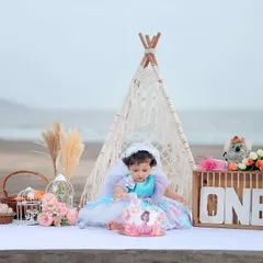 A boho-chic first birthday cake smash on the beach, featuring a macrame teepee and pampas grass against the ocean backdrop.