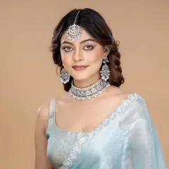 A model looks directly at the camera, showcasing a stunning silver-toned choker, maang tikka, and earrings set. The clean background and confident pose make this a perfect image for a modern ethnic jewellery catalogue.