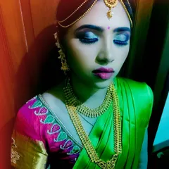 A detailed shot of a South Indian bridal or festive look. The focus is on the dramatic blue and silver smokey eye, paired with a pink lip, traditional gold jewelry, and a matha patti hair accessory.