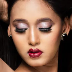 A close-up beauty shot in color, focusing on the model's metallic eyeshadow and bold red lips. The lighting perfectly captures the makeup's texture and pigment.