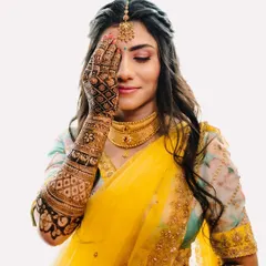 A beautiful portrait focusing on the bride's intricate Mehendi design. The vibrant yellow of her saree contrasts perfectly with the deep color of the henna, celebrating this traditional art form.