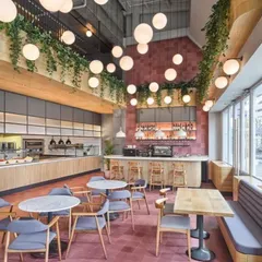 We designed this spacious, double-height cafe to feel vibrant and full of life. The design features a bold pink tiled floor, an array of spherical pendant lights for dramatic effect, and hanging greenery to soften the industrial architecture, creating an energetic and welcoming atmosphere for customers.