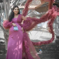 A stylish outdoor portrait featuring a dramatic ruffled gown. The mom-to-be holds a pair of baby shoes, blending high fashion with a sweet, personal touch.