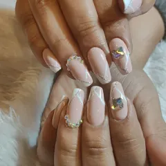 A sophisticated nude and white design on almond-shaped nails, accented with silver glitter lines and stunning iridescent and pearl-like rhinestones.