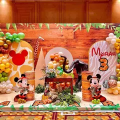 Welcome to a Mickey Mouse jungle safari adventure! This expansive backdrop brings the wild indoors with a wood-paneled wall, lush balloon garlands in earthy tones, and beloved characters like Mickey and Pluto ready for exploration. It's a perfect example of how I transform a space into a story.