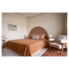 In this bedroom, we designed a custom arched, channel tufted headboard and a minimalist wooden armchair. The space is a fusion of rustic and elegant styles, using honest materials to create a peaceful haven.