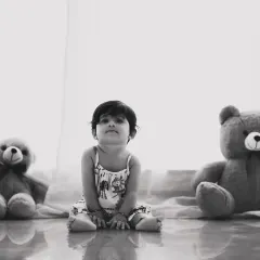 A simple, classic portrait of a baby sitting between two teddy bears. The black and white treatment gives it a timeless, nostalgic quality.