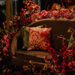 For this sangeet, I designed a cozy yet luxurious seating area by surrounding a plush sofa with a forest of red flowers. The baroque-style cushion adds a touch of old-world romance to the modern setup.