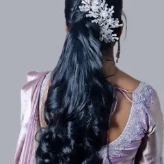 A modern and sleek half-up ponytail with soft waves. The look is elevated with a striking white crystal accessory, making it a great choice for a contemporary party look.