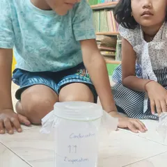 Two children patiently watch their mini water cycle in a jar. They can see the evaporation and condensation happening right before their eyes, making a big concept easy to understand.