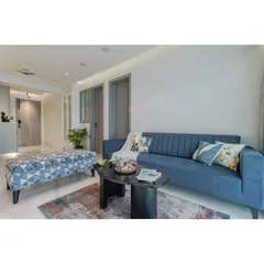 Comfort is key in any living room design. This view showcases the plush, channel-tufted blue sofa, paired with a geometric-print ottoman and a modern black coffee table. It’s a practical and stylish setup for everyday living.