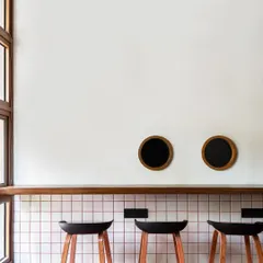 Simplicity and clean lines define the bar seating area. White grid tiles with red grouting, a simple wooden counter, and modern black stools create a look that is both retro-inspired and distinctly contemporary.