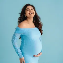 A happy, candid-style portrait of a mother-to-be in a light blue gown.