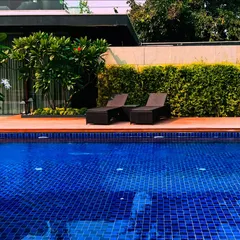 A perfect poolside scene with two lounge chairs on a wooden deck, overlooking the sparkling blue water. The lush green hedge provides privacy and a natural backdrop.