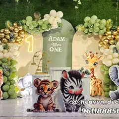 A premium jungle safari theme for a first birthday, featuring an elegant balloon arch in gold and sage green. The setup includes multiple cute animal cutouts like a lion, tiger, and elephant, with a light-up number '1' and themed plinths.