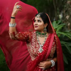 A dynamic and joyful shot of a model in a red lehenga, perfect for a reception or sangeet. She is wearing a stunning emerald and American Diamond necklace set that adds a touch of modern glamour.