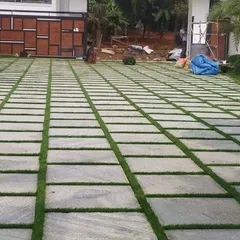 A work-in-progress shot of a large driveway. The stone pavers have been laid, and the gaps are now ready to be filled with soil and grass seed or sod to create the final green-striped effect.