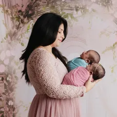 Double the joy. A beautiful mother holding her newborn twins, one in pink and one in blue, in a dreamy, floral setting.