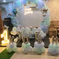 Celebrating a first birthday with a modern pastel theme. This decor features a half-arch of balloons, a 'Happy Birthday' neon sign, a light-up number '1' marquee, and the baby's name in silver foil balloons for a personalized touch.