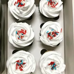 Simple, classic, and delicious. This top-down view shows six of our homemade cupcakes with fluffy white frosting roses and a dash of red and blue sprinkles, ready to brighten your day.