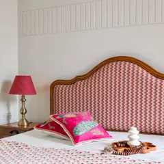 A bedroom design featuring a custom bed with a curved, wood-framed headboard upholstered in a vibrant pink chevron fabric. The wall behind features subtle vertical fluting for added texture.