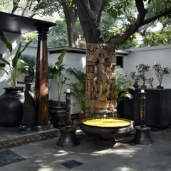A corner of the courtyard featuring a large stone sculpture of Vishnu and a traditional bronze 'Uruli' filled with flowers. This space is a "museum without walls," where art and artifacts are displayed in an open, natural setting.