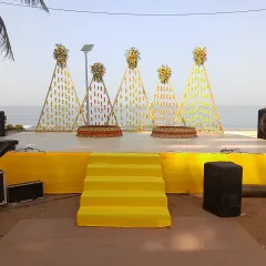 This Haldi stage was designed for a beach event, using bright yellow fabric and creative backdrops made of marigold strings in a triangular pattern. It's a modern take on traditional decor.