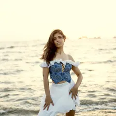 A full-length portrait against the sea at sunset. This image highlights the entire outfit, a custom blue and white dress, showing how it moves and looks in a natural, beautiful environment.