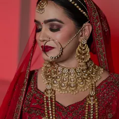 This profile shot showcases the harmony between the makeup and the heavy bridal jewelry. The defined eyes and rich red lipstick create a look of pure elegance.