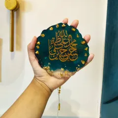 This is a custom resin car hanging featuring beautiful Islamic calligraphy. This piece includes the Panjatan names in gold against a deep teal and clear resin base, accented with gold flakes for an elegant finish. It's a meaningful accessory for your car's interior.