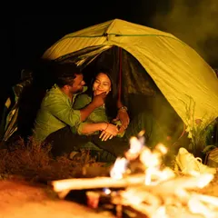 A magical night under the stars. The couple shares an intimate moment inside a tent, illuminated by the warm, flickering light of a campfire. This is the perfect setup for a cozy, adventurous pre-wedding shoot.