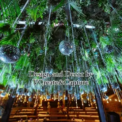 A stunning ceiling treatment for an outdoor sangeet, featuring a dense canopy of green leaves and dozens of hanging disco balls that sparkle in the light.