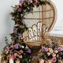 A close-up of the peacock chair, adorned with a lush floral garland and surrounded by candles. This creates a beautiful and regal focal point for a baby shower, perfect for photos.