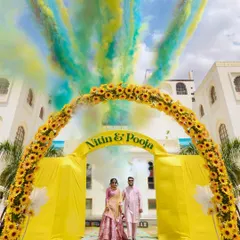 A spectacular Haldi ceremony entrance, with the couple framed by a sunflower arch and vibrant color smoke. We love capturing the energy and joy of pre-wedding festivities.