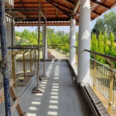 The play of light and shadow is already evident on this unfinished balcony, as sunlight filters through the temporary scaffolding and roof structure.