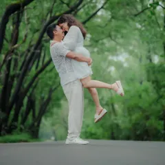 A joyful and spontaneous moment on a road surrounded by a canopy of green trees. The groom lifts his bride-to-be in a playful embrace, capturing pure happiness.