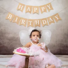 A full portrait of a baby girl dressed as a fairy, completely covered in pink frosting during her very first cake smash.