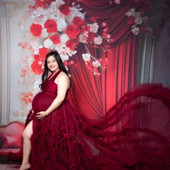 A glamorous maternity portrait of a mother-to-be in a stunning, floor-sweeping red gown against a dramatic floral backdrop.