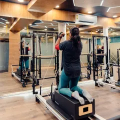 Here, a client uses the reformer box and arm straps on the Cadillac tower. This setup allows for targeted upper body work while maintaining core stability.