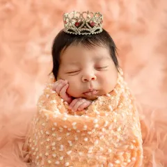 A classic newborn portrait of a sleeping baby girl, swaddled snugly and wearing a tiny, delicate crown. My newborn sessions are always handled with the utmost care and safety for your little one.