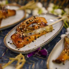 A skewer of glazed salmon, sprinkled with black and white sesame seeds. This appetizer combines sweet and savory flavors with a beautiful presentation, perfect for an elegant cocktail party or corporate event.