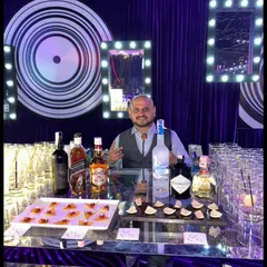 Our founder Sid behind a sleek, modern bar at a private party. The setup includes a mirrored bar front, vanity lights, and a tray of our signature edible cocktails.