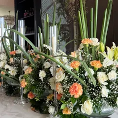 A close up of the stunning floral centerpieces on the dining table. We used a mix of white daisies, peach carnations, and tall green leaves, with slender candles interspersed for a soft, ambient glow.