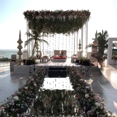A stunning seaside mandap with a mirrored aisle reflecting the sky. The structure is adorned with a lush floral canopy, creating a space where vows feel as infinite as the ocean.