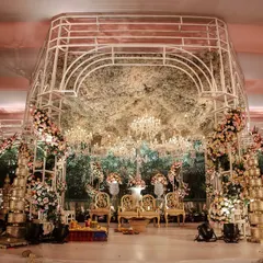 A modern, structural mandap with a canopy of dense, rustic foliage and dozens of hanging crystal chandeliers. The design blends natural textures with glamorous elements for a unique and romantic effect.