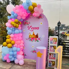 A princess-themed first birthday decoration for Zeera, set up on a terrace. The design includes a custom arch backdrop with her name, a balloon garland, "BABY" blocks, and a light-up number '1'.